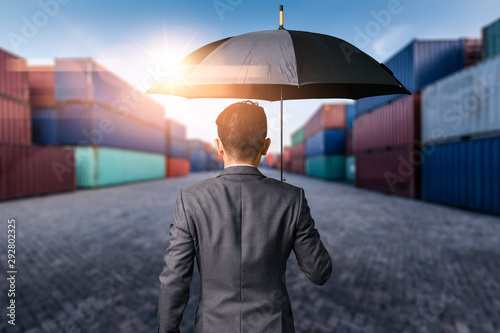 The abstract image of the Businessman is spreading umbrella during sunrise overlay with container yard image. The concept of transportations, business, insurance, and protection.