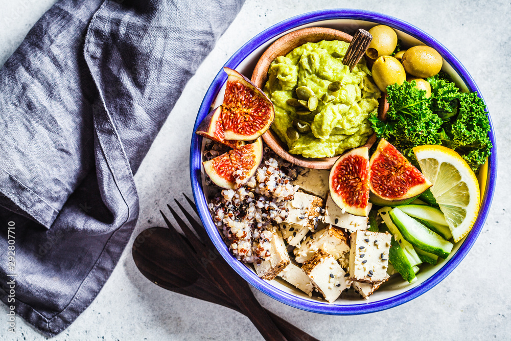 Buddha bowl with quinoa, tofu, kale, fig and guacamole hummus in a white plate, top view. Buddha bowl with quinoa, tofu, kale, fig and guacamole hummus in a white plate, top view.