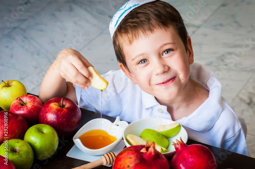 Cute adorable Caucasian Jewish child dipping an apple piece into honey on the Jewish New Year holiday of Rosh Hashanah concept image.