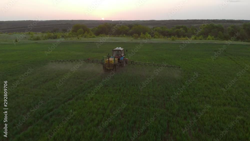 Aerial view of farming tractor spraying on field with sprayer, herbicides and pesticides at sunset. Farm machinery spraying insecticide to the green field, agricultural natural seasonal spring works. Aerial view of farming tractor spraying on field with sprayer, herbicides and pesticides at sunset. Farm machinery spraying insecticide to the green field, agricultural natural seasonal spring works.