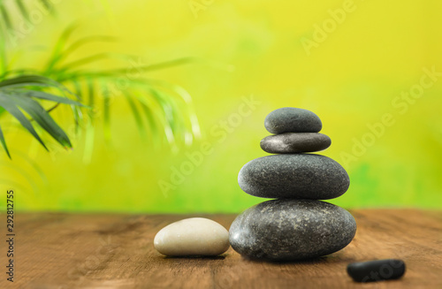 Table with stack of stones and blurred green leaves on background, space for text. Zen concept