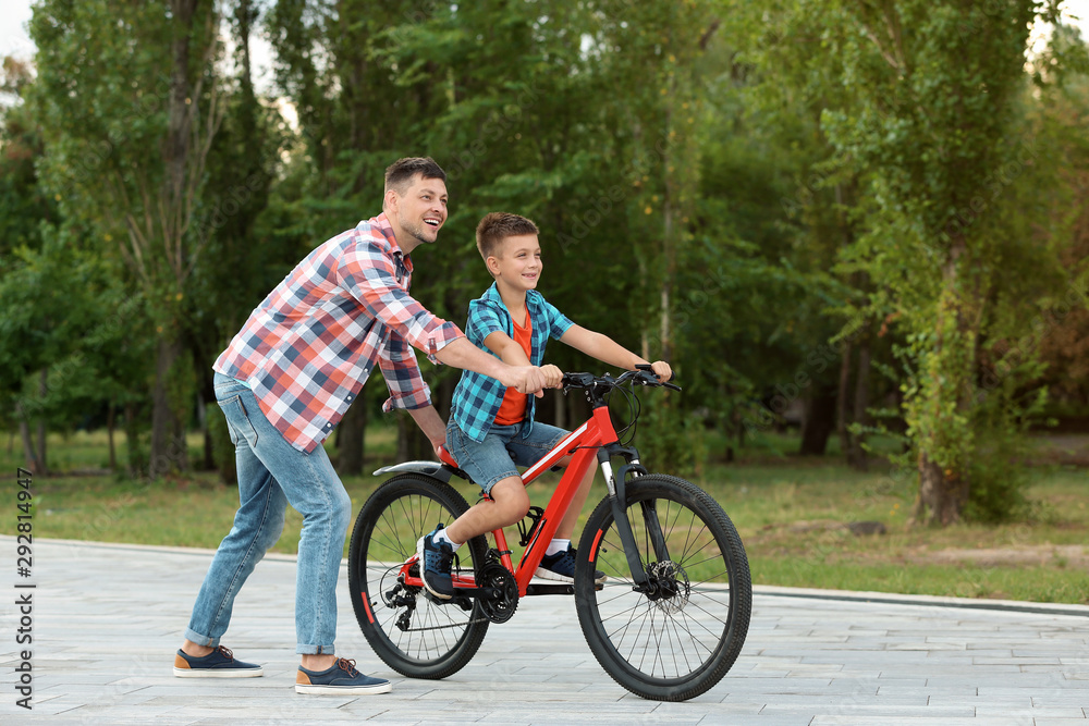 Dad teaching son to ride bicycle in park Dad teaching son to ride bicycle in park