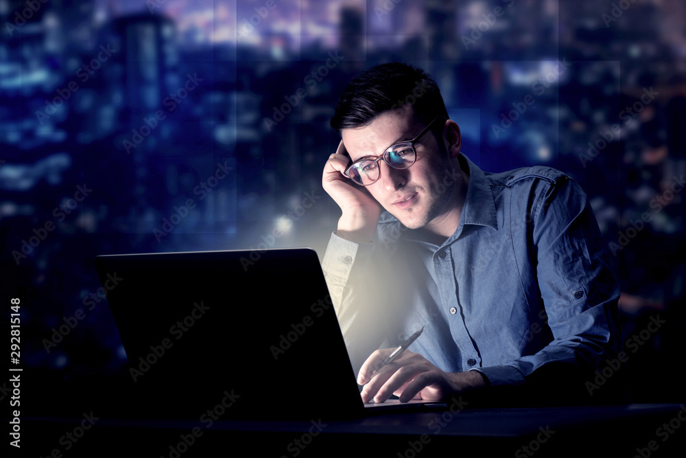 Young handsome businessman working late at night in the office with blue lights in the background Young handsome businessman working late at night in the office with blue lights in the background