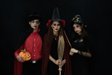 Three Asian people model dressed as Dracula and witch and a witch's hat costume smile and acting on Halloween party standing with a dark background.