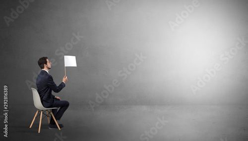 Canvas Print Businessman staying in an empty grey dark room with stuffs on his lap