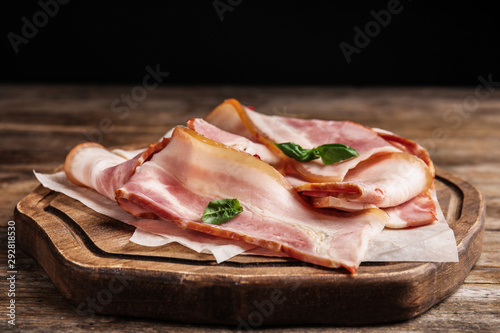 Board with slices of raw bacon on wooden table, closeup