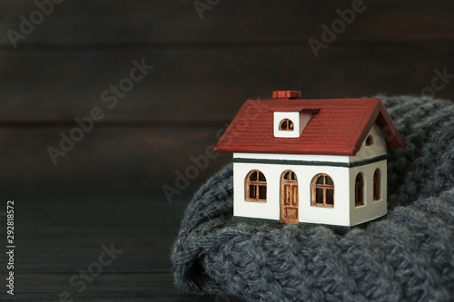 House model and scarf on black table against wooden background, space for text. Heating efficiency