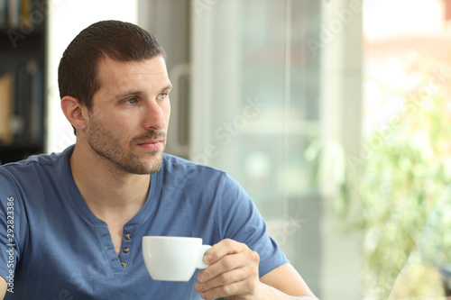 Pensive man holding coffee cup looks away through a window