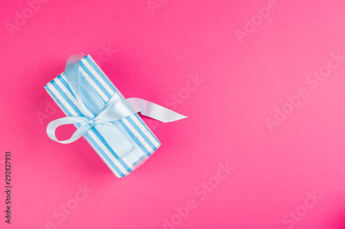 Top view of a decorated present with a bow on pink background
