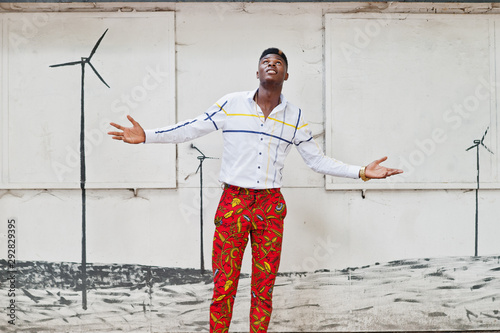 Portrait of handsome stylish african american model man in red throusers and white shirt. Raised his hands to the sky. photo