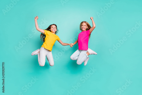 Full length body size photo of two casual cute childish girls people rejoicing with having won something hand in hand while isolated with teal background