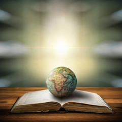 An old globe lying on an open book against the background of bookshelves in a library. Selective focus. Retro style. Science, education, travel, vintage background. History and geography team.