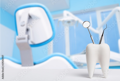 Oral dental hygiene. Healthy white tooth and dentist mirror with explorer probe instrument against blurred dentist Office background with dental chair and lamp.