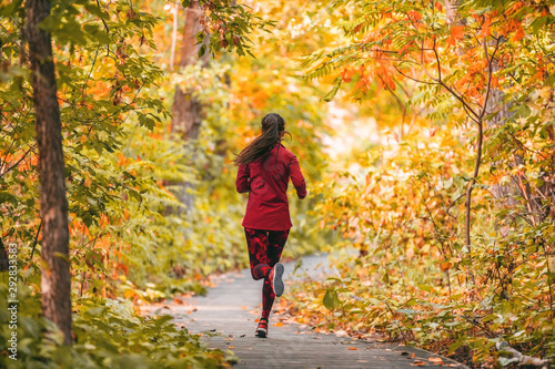 Run woman jogging in outdoor fall autumn foliage nature background in forest. Trail running runner athlete training cardio outdoors, orange colors tree leaves.