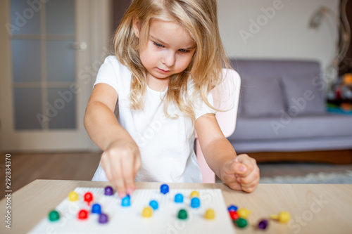 Little blonde girl in a white tshirt playing with plastic multicolor mosaic at home or preschool. Early education concept.
