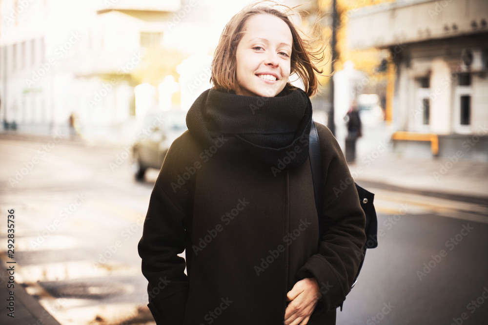 Young beautiful happy girl woman in a coat and scarf on a sunny autumn street