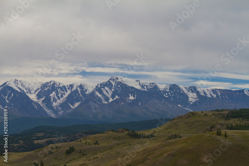 Snow top in Altai mountains. Bottom view. Summer travel concept. Dark day with clouds.