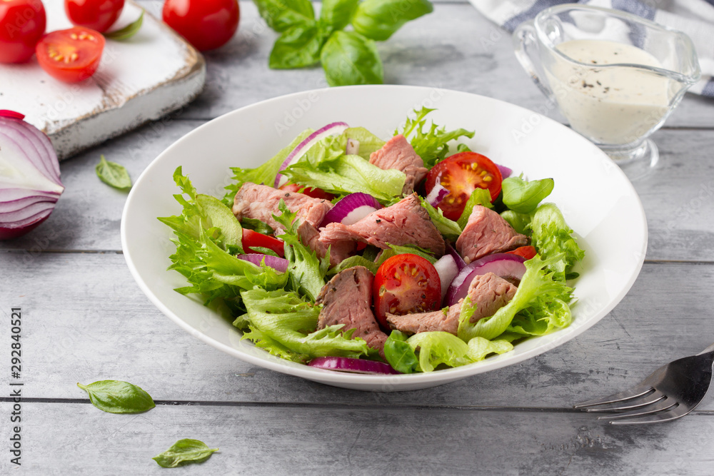 Salad with roast beef, tomato, onion, lettuce and mustard sauce on light background. Delicious healthy lunch with meat, diet food