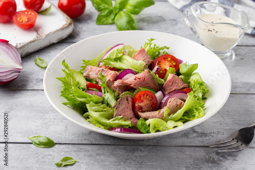 Salad with roast beef, tomato, onion, lettuce and mustard sauce on light background. Delicious healthy lunch with meat, diet food
