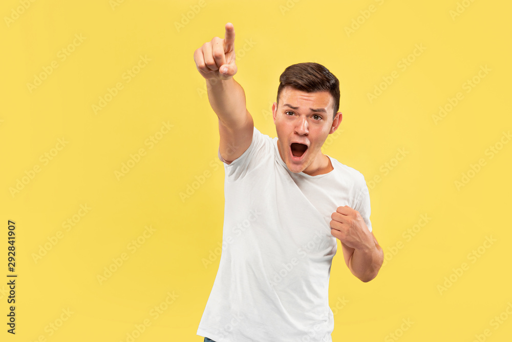 Caucasian young man's half-length portrait on yellow studio background. Beautiful male model in shirt. Concept of human emotions, facial expression, sales, ad. Pointing on and looks happy. Caucasian young man's half-length portrait on yellow studio background. Beautiful male model in shirt. Concept of human emotions, facial expression, sales, ad. Pointing on and looks happy.