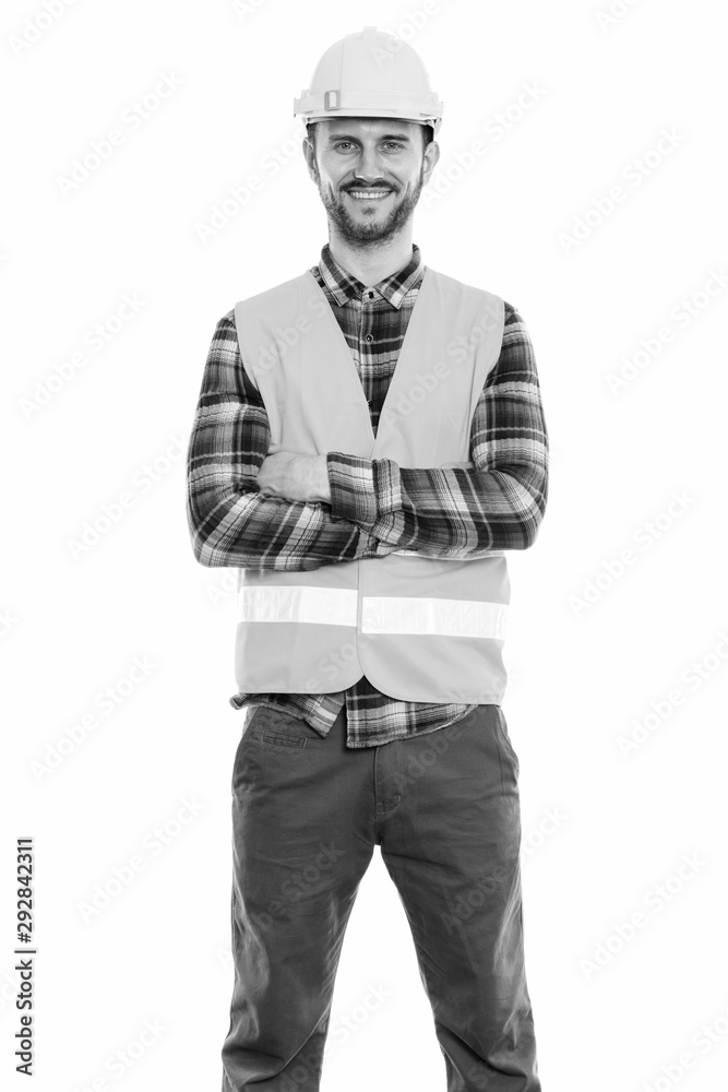 Fototapeta premium Studio shot of happy young man construction worker smiling and standing with arms crossed