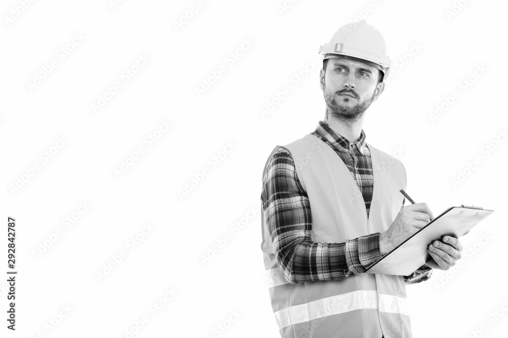 Studio shot of young man construction worker writing on clipboard while thinking Studio shot of young man construction worker writing on clipboard while thinking