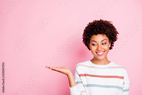 Photo of pretty dark skin wavy lady holding on open palm new cheap product advising buyers wear striped pullover isolated pastel pink color background