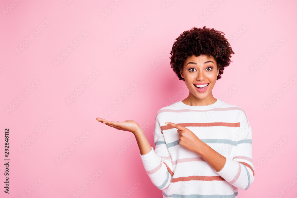 Photo of pretty dark skin wavy lady indicating finger on open palm advising new amazing cheap product wear striped pullover isolated pastel pink color background Photo of pretty dark skin wavy lady indicating finger on open palm advising new amazing cheap product wear striped pullover isolated pastel pink color background