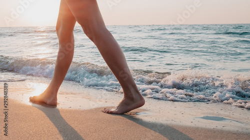 Legs of a young slender girl in black short dress walk along promenade of the sandy sea shore