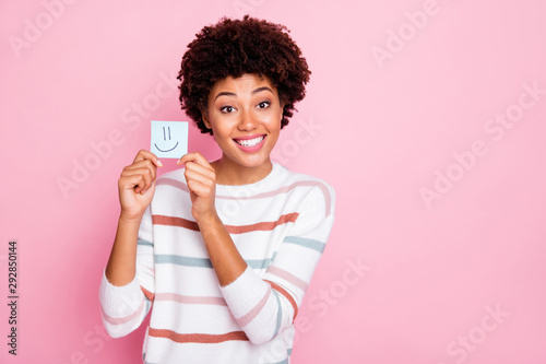 Photo of cheerful charming cute nice girlfriend black skinned holding piece of paper with emoji drawed on wearing white striped sweater isolated over pastel pink color background