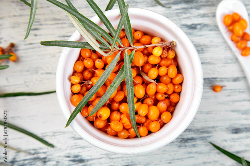 Natural, organic sea buckthorn berry in bowl and a on white wooden background. Branch of sea buckthorn. Top view.