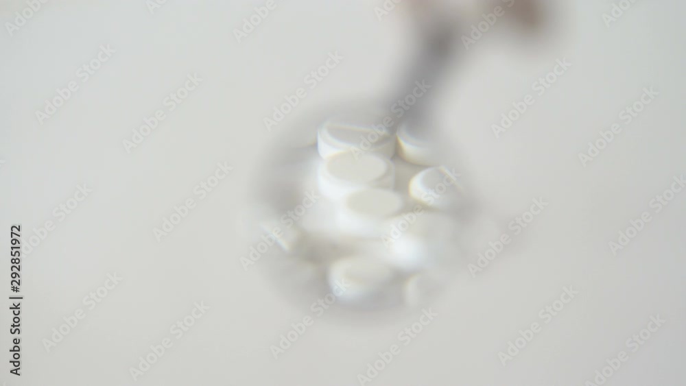 White round pills. Pills lie on a white surface. Hand with a magnifier. Looking through the glass. Medical product. The cure for the disease. Close-up. White round pills. Pills lie on a white surface. Hand with a magnifier. Looking through the glass. Medical product. The cure for the disease. Close-up.