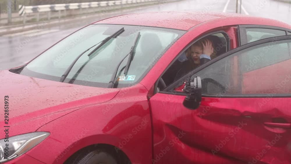 Close-up of a frightened girl sitting in the car after an accident in the rain, she holds her head and cries. Slow motion. Car accident on the road.