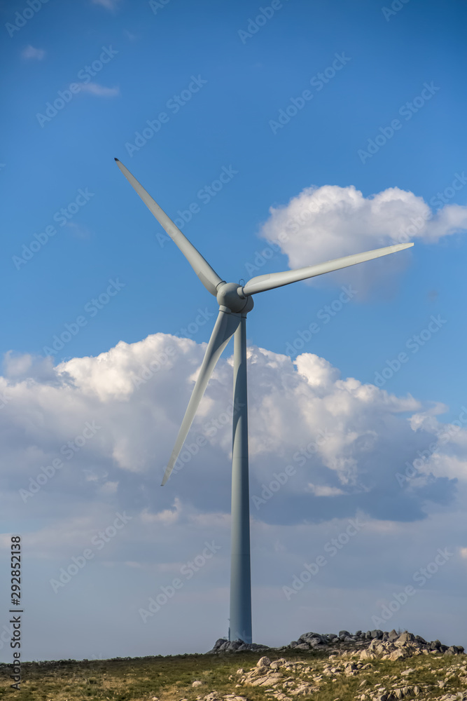View of a wind turbine on top of mountains, blue sky as background View of a wind turbine on top of mountains, blue sky as background