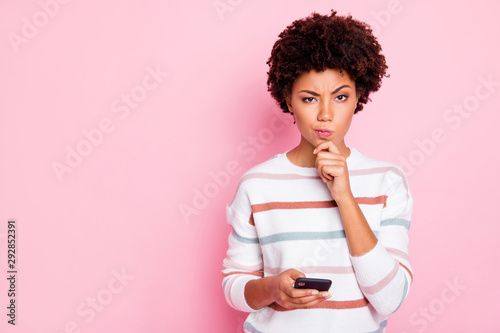 Photo of pretty dark skin lady holding telephone deciding what comment to write hand touch chin wear white striped pullover isolated pastel pink color background photo