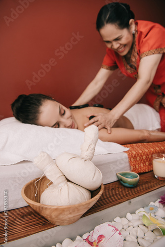 selective focus of herbal balls and asian masseur doing hot stone massage