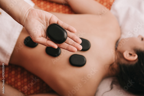 cropped view of masseur doing hot stone massage to woman in spa salon