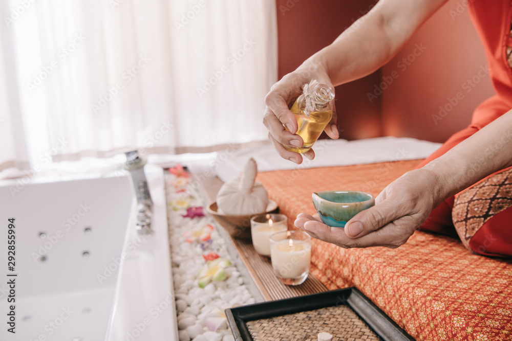 cropped view of masseur sitting on massage mat and pouring fragrance oil to bowl cropped view of masseur sitting on massage mat and pouring fragrance oil to bowl