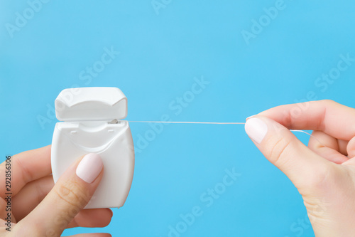 Woman fingers holding new white plastic container with dental floss on pastel blue background. Teeth hygiene concept. Closeup. Point of view shot. photo