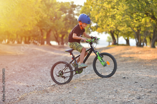 Happy kid boy of 7 years having fun in autumn park with a bicycle on beautiful fall day. Active child wearing bike helmet