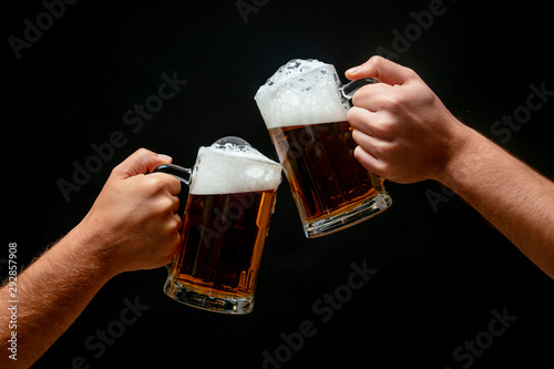 Hands toasting with beer on black background