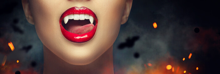 Sexy Vampire Woman's red bloody lips close-up. Vampire girl licking fangs with tongue. Fashion Glamour Halloween art design. Close up of female vampire mouth, teeth. Vampire woman teeth closeup
