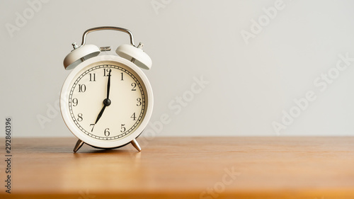 White alarm clock on brown wood desk and cream wallpaper textured background with copy space
