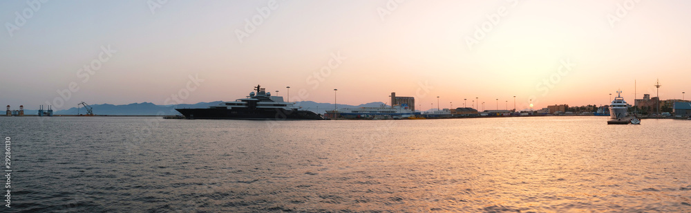 AUG 2019 seascape of port of Cagliari at sunset with big yacht and boat with container - Sardinia.