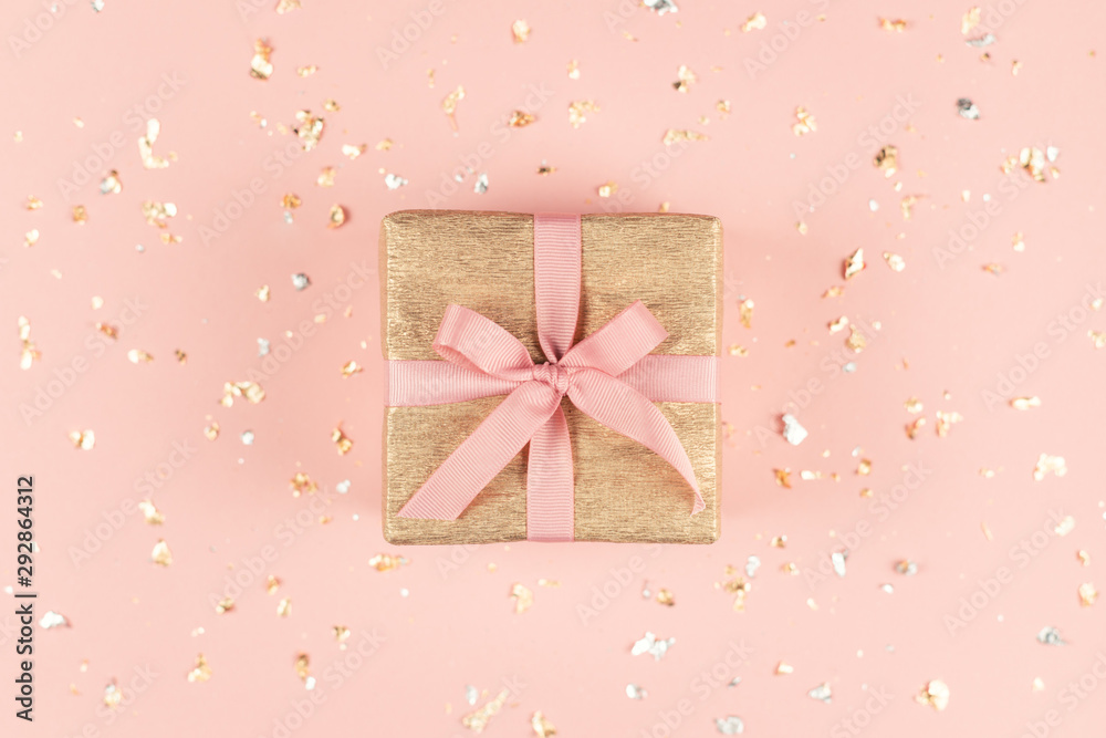 Golden gift box with pink bow on the pink background with golden and silver sparkles.