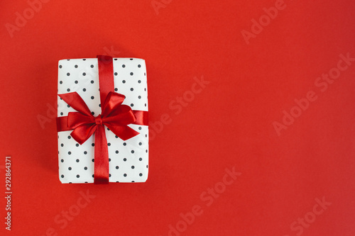 Gift box wrapped in black polka-dot white paper with red bow on red background.