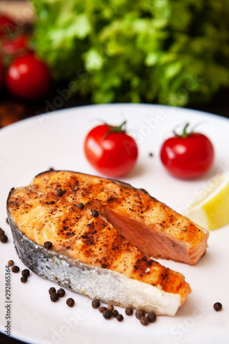 Salmon cooked on the grill arranged on a plate with tomatoes and black pepper