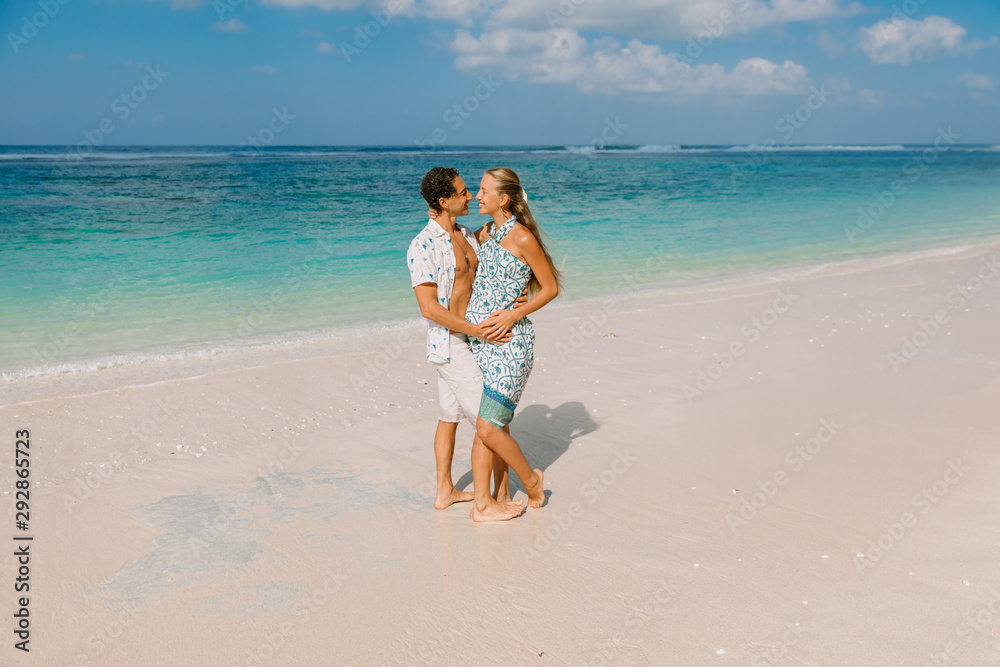Young pregnant woman with husband relaxing at paradise beach. Happy couple in tropics Young pregnant woman with husband relaxing at paradise beach. Happy couple in tropics