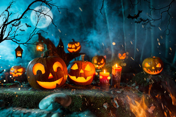 Halloween pumpkins on dark spooky forest with blue fog in background.