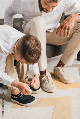 cropped view of father teaching son to tying shoelaces at home